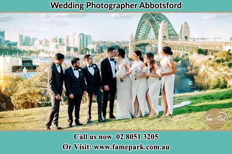 Photo of the Groom and the Bride kissing with the entourage near the bridge Abbotsford NSW 2046