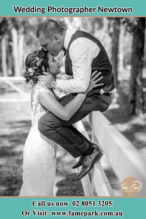 Photo of the Groom sitting on the fence while kissing the Bride on the forehead Newtown NSW 2042